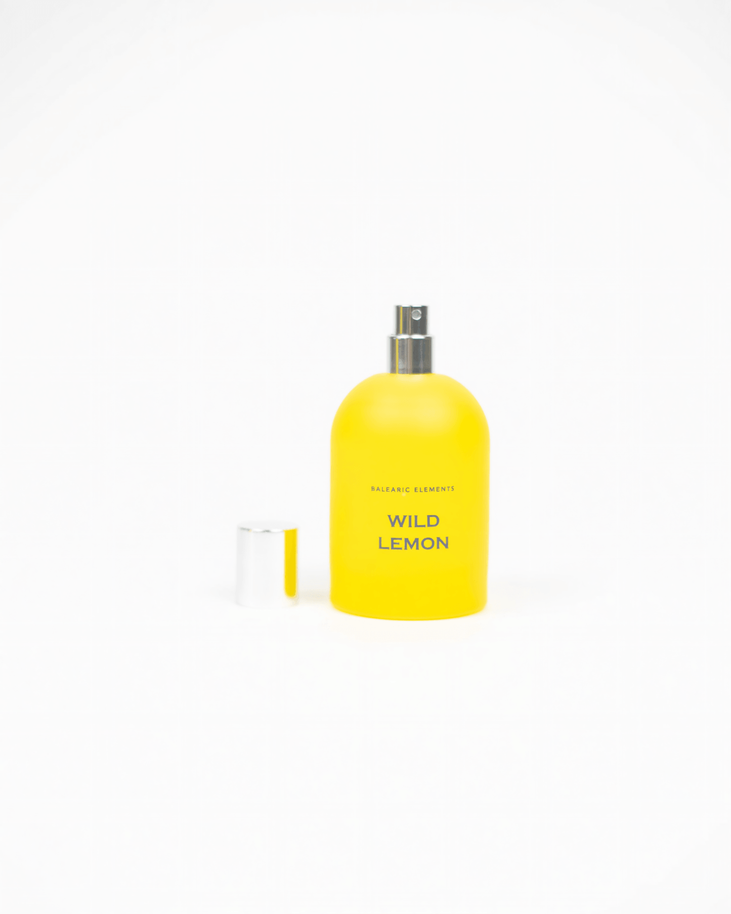 A bright yellow perfume bottle labeled 'WILD LEMON' with a silver spray top, shown on a clean white background with the cap placed to the left.