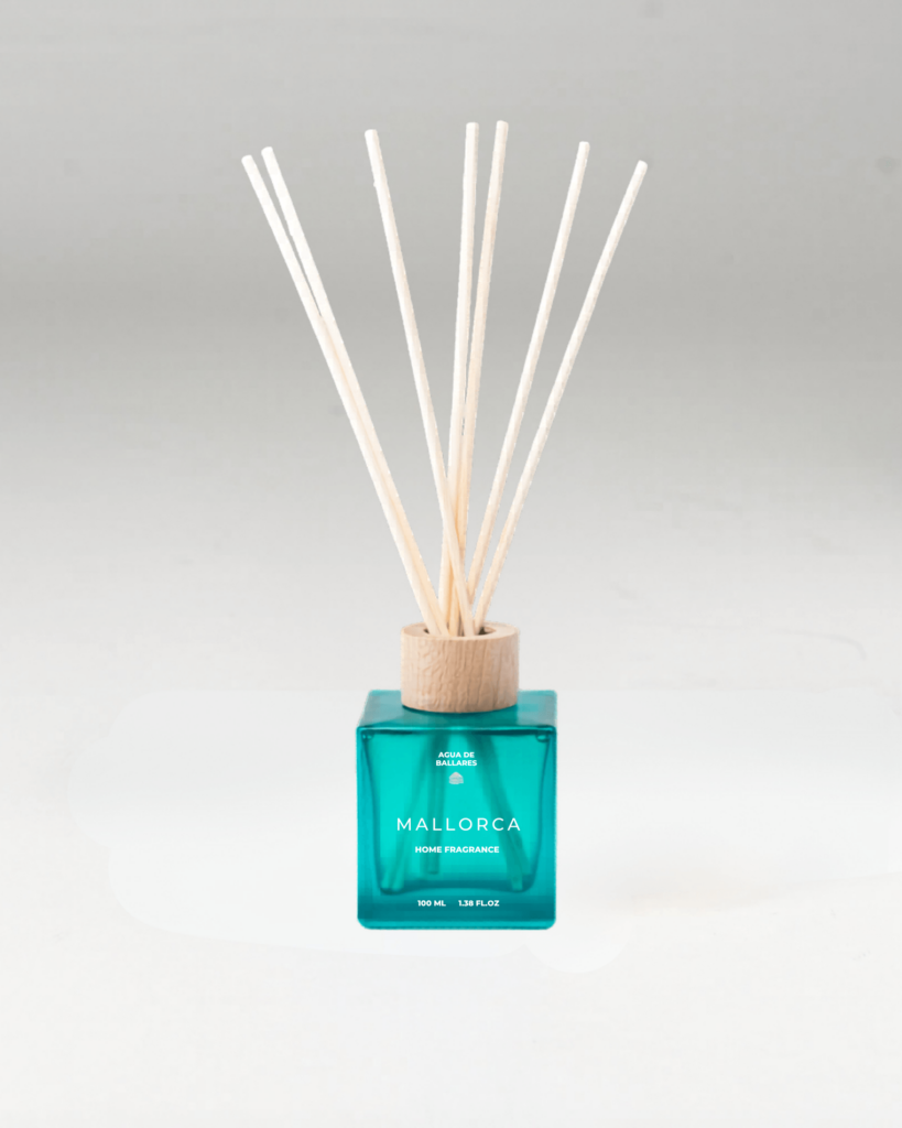 A reed diffuser bottle with a translucent teal-blue glass body, a light natural wood collar, and multiple pale reed sticks, labeled MALLORCA, on a clean light gray background.