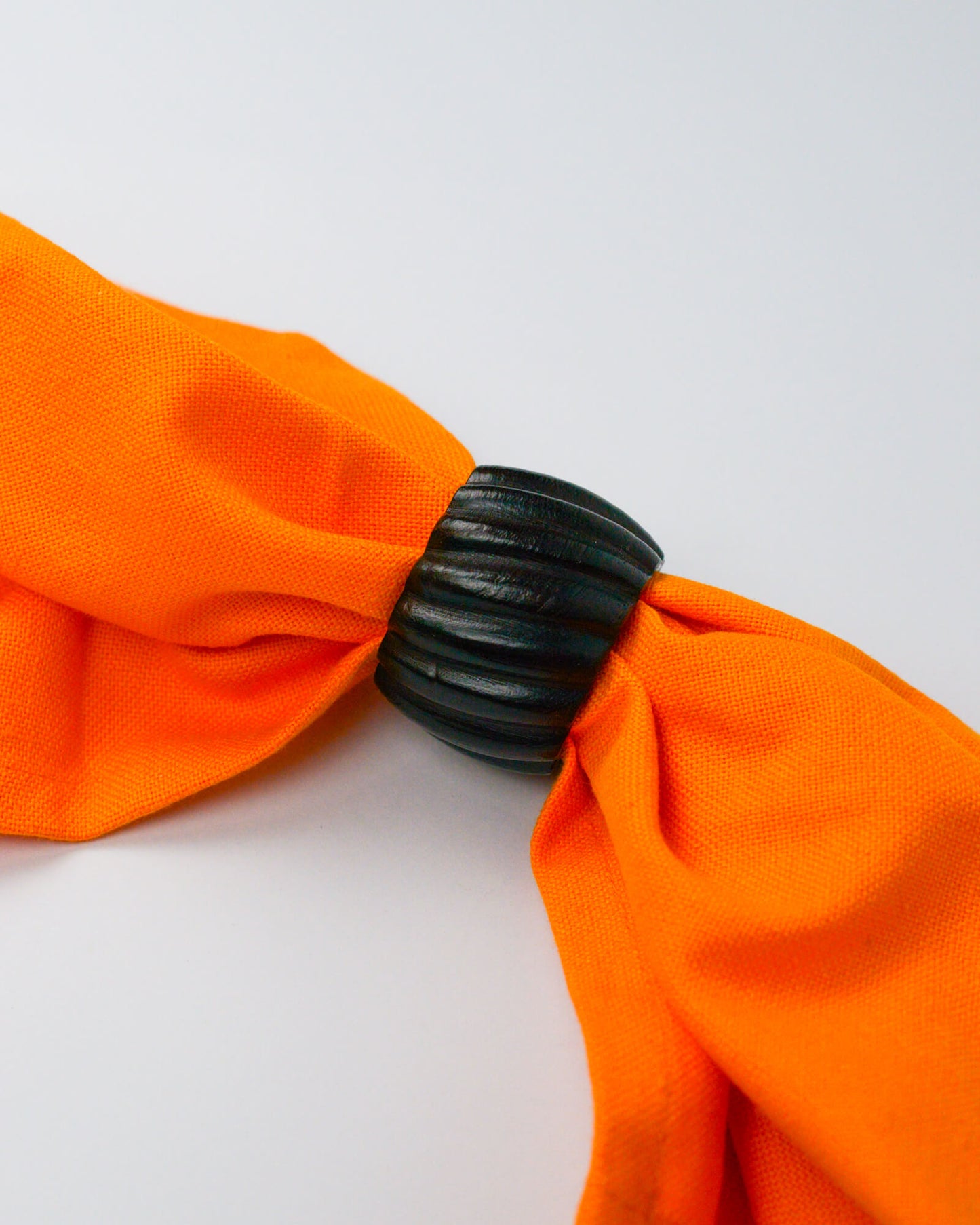 Orange cotton napkin held with a dark wooden ribbed wooden napkin ring on a white background