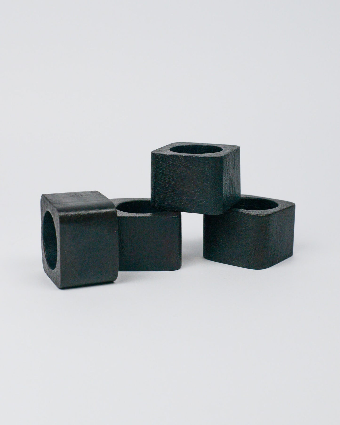 Four dark wood square-shaped napkin rings on a white background