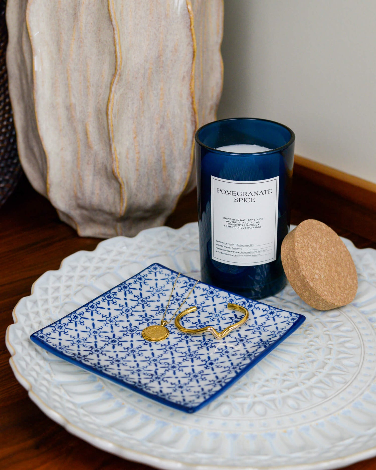 Blue glass jar candle resting on a decorative plate with a blue and white square trinket tray in the foreground