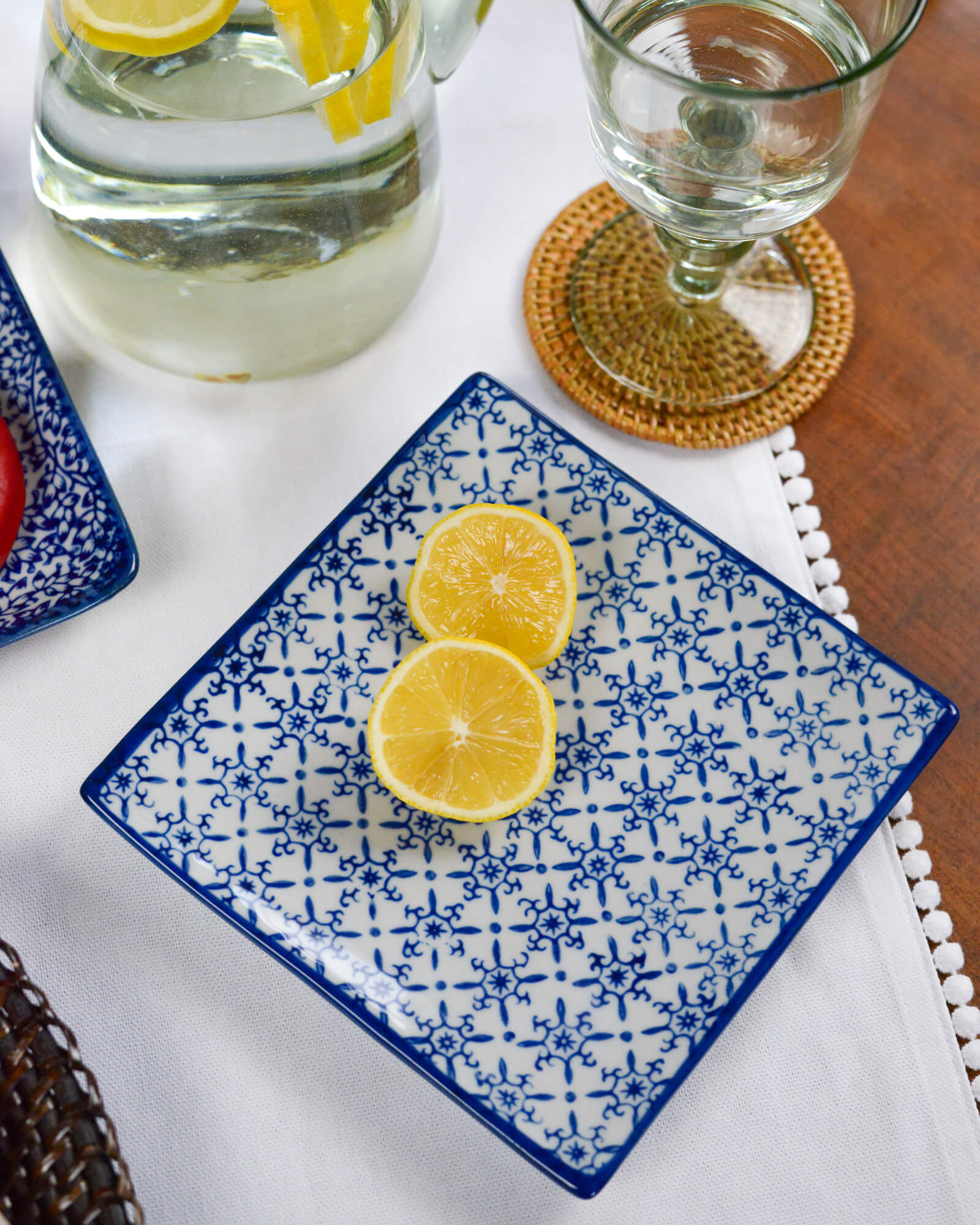 Blue and white patterned plate with lemon slices on a table with a glass of water and coaster.