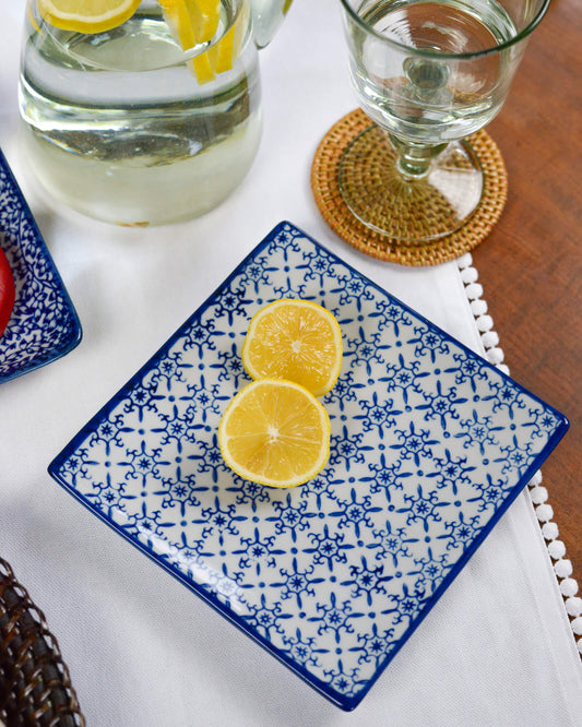 Blue and white patterned plate with lemon slices on a table with a glass of water and coaster.