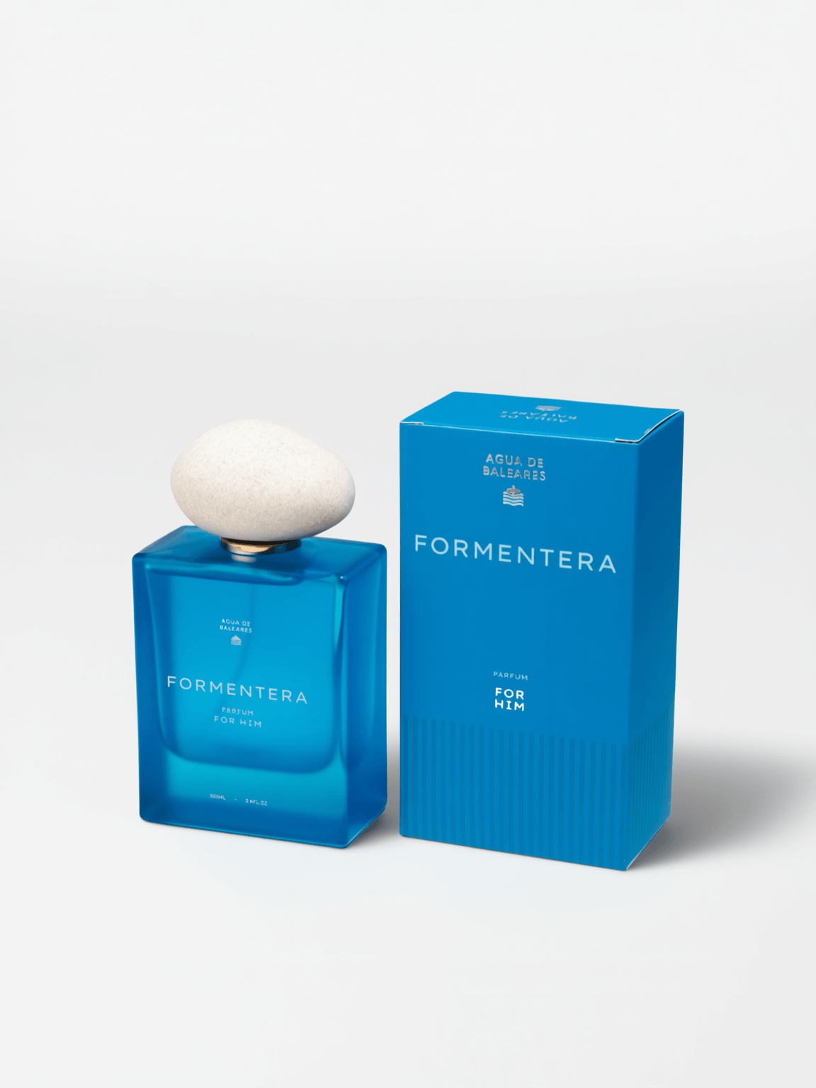 A bottle of Formentera Parfum next to its blue packaging box, featuring a white stone cap on the bottle, set against a clean white background.