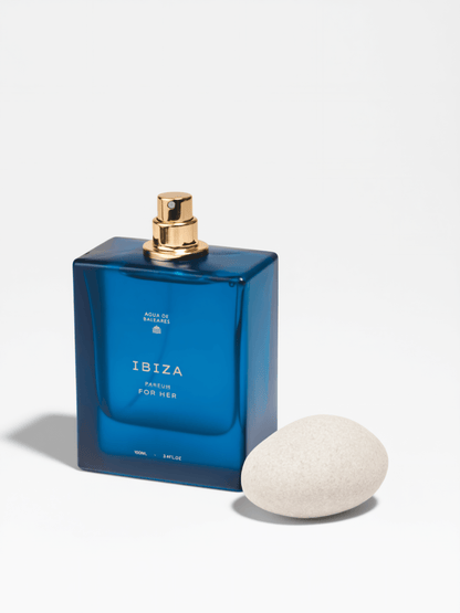 A blue rectangular perfume bottle with pebble like cap, and gold atomiser labeled 'IBIZA' sits on a white background 