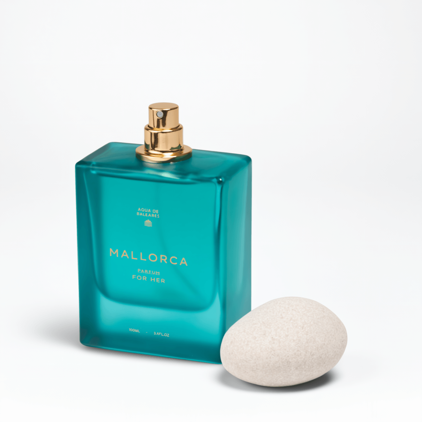 A teal glass perfume bottle labeled MALLORCA PARFUM with a gold spray top, shown next to a smooth white stone on a clean white background.