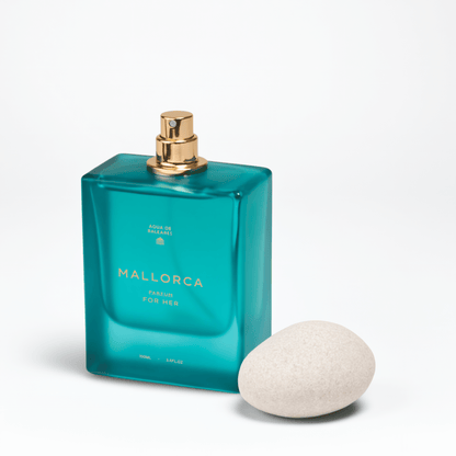 A teal glass perfume bottle labeled MALLORCA PARFUM with a gold spray top, shown next to a smooth white stone on a clean white background.