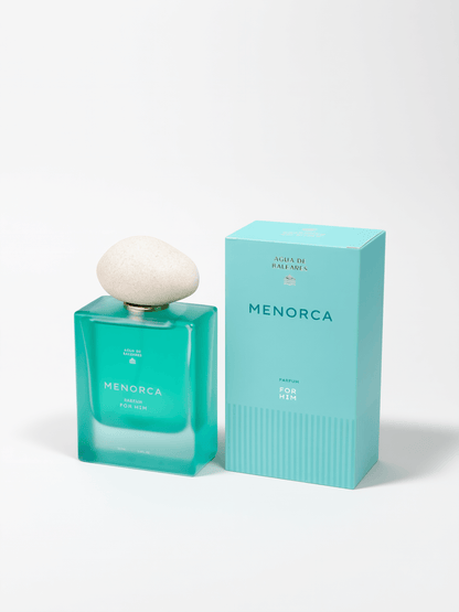 A bottle of Menorca Parfum in a translucent turquoise glass bottle with a white stone-like cap, shown next to its matching turquoise packaging box on a white background.