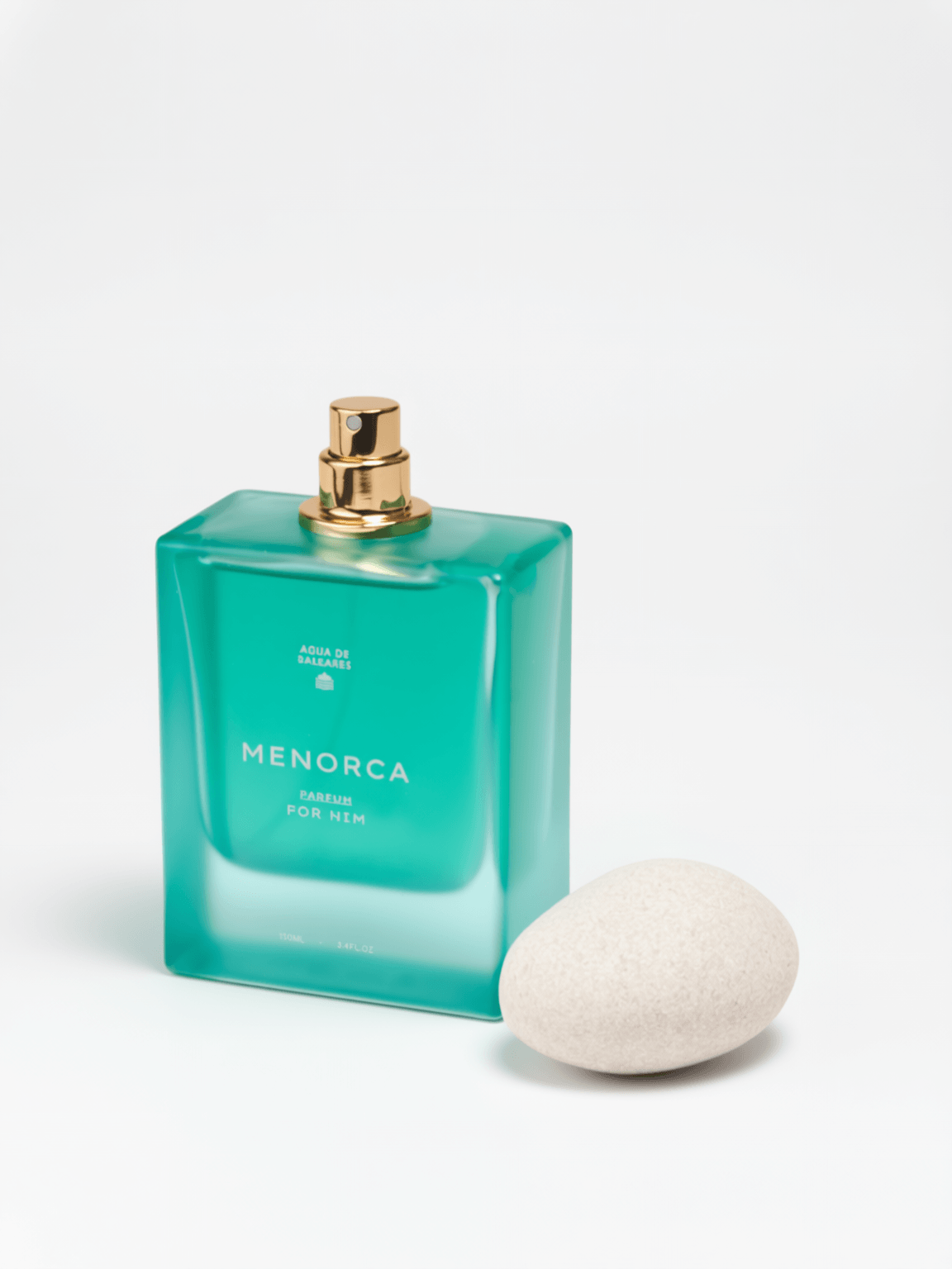 A rectangular translucent aqua-green perfume bottle labeled MENORCA with a gold spray top, photographed on a clean white background with a smooth off-white stone beside it.