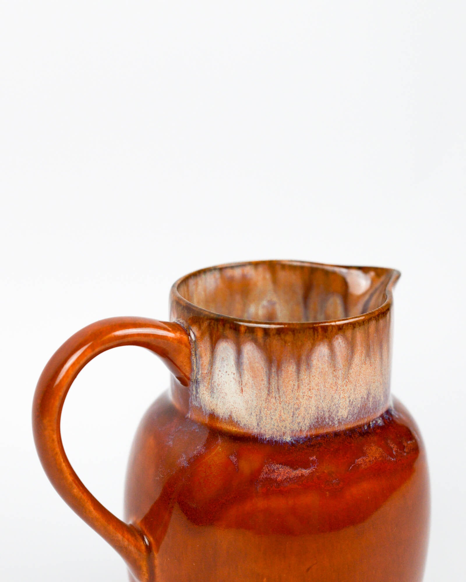 Detail from a burnt orange ceramic pitcher on a white background
