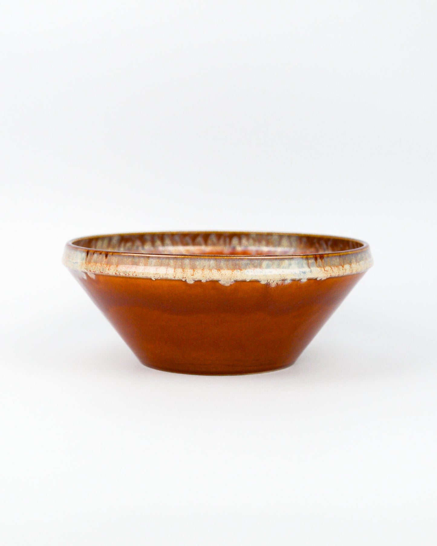 Ceramic serving bowl with a burnt orange and beige glazed rim on a white background