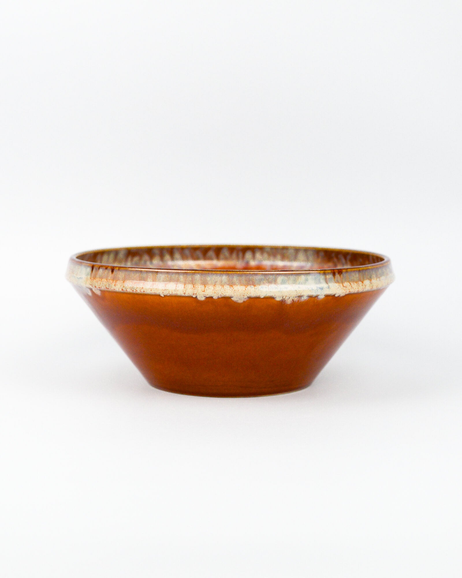 Ceramic serving bowl with a burnt orange and beige glazed rim on a white background