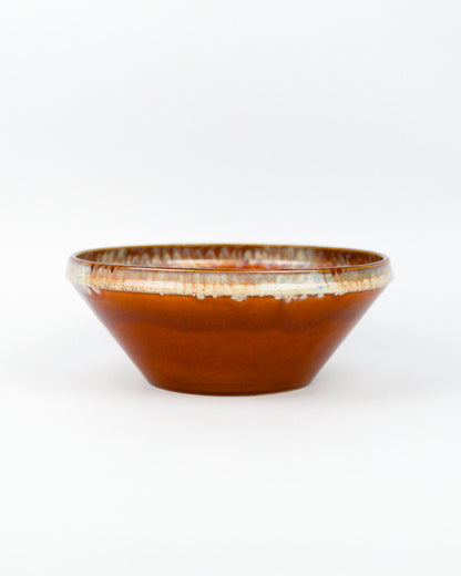 Ceramic serving bowl with a burnt orange and beige glazed rim on a white background