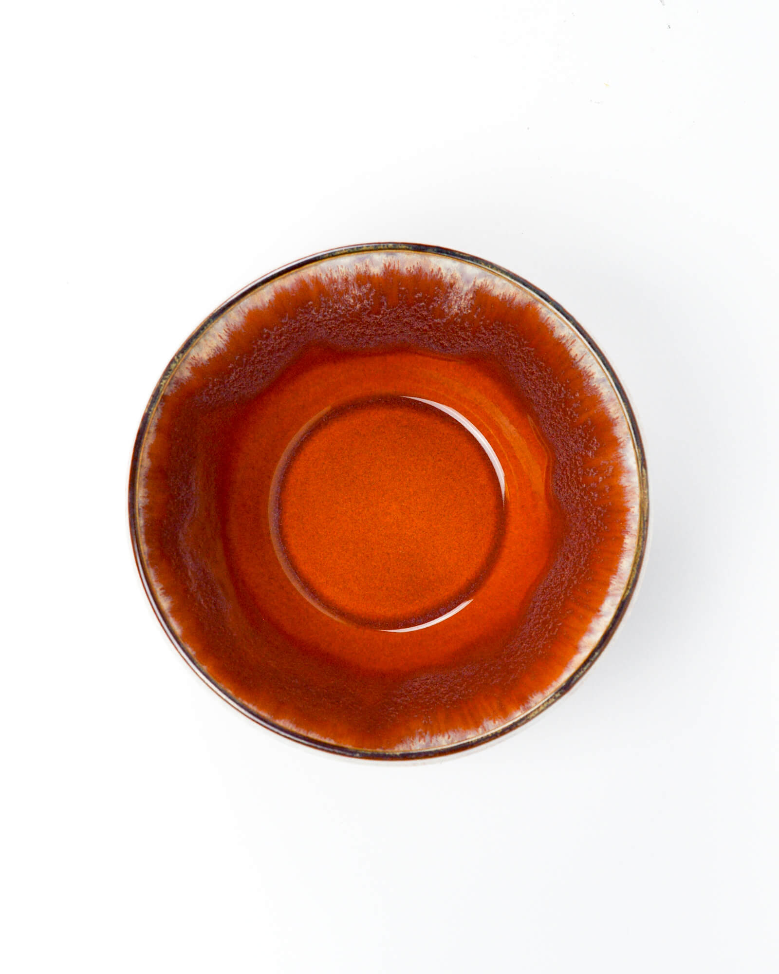 Arial shot of a ceramic serving bowl with a burnt orange and beige glazed rim on a white background
