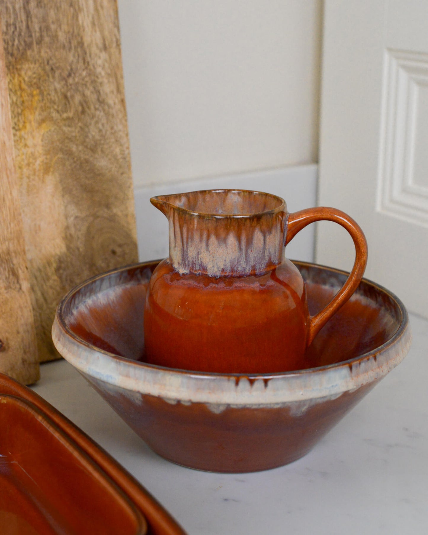 Ceramic pitcher and bowl with burnt orange, caramel glaze on a white marble surface