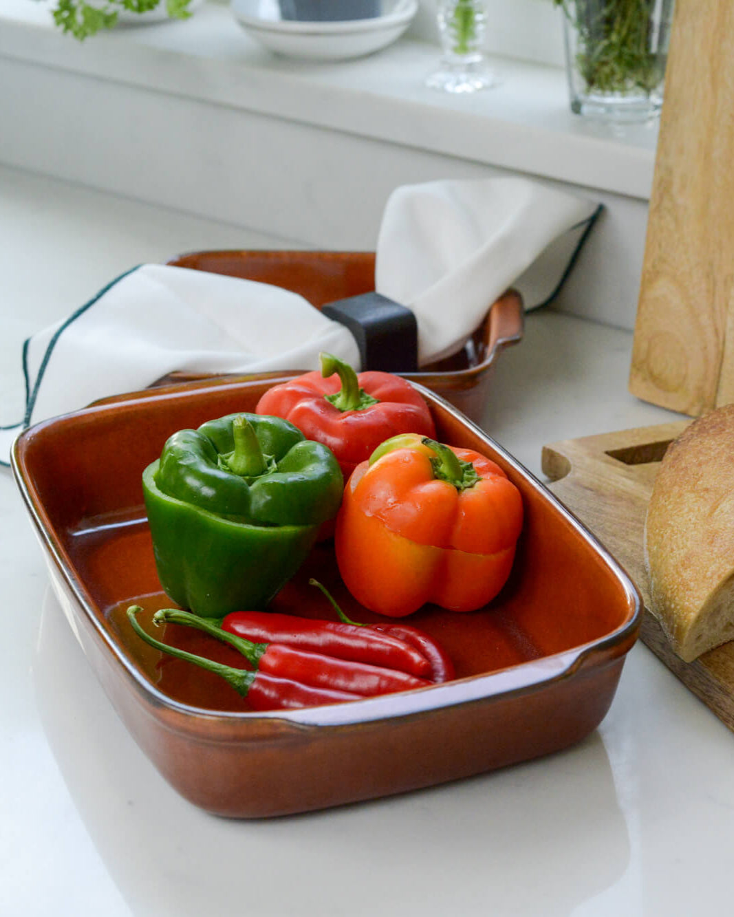 Colorful bell peppers in a caramel coloured ceramic stoneware dish on a kitchen counter.