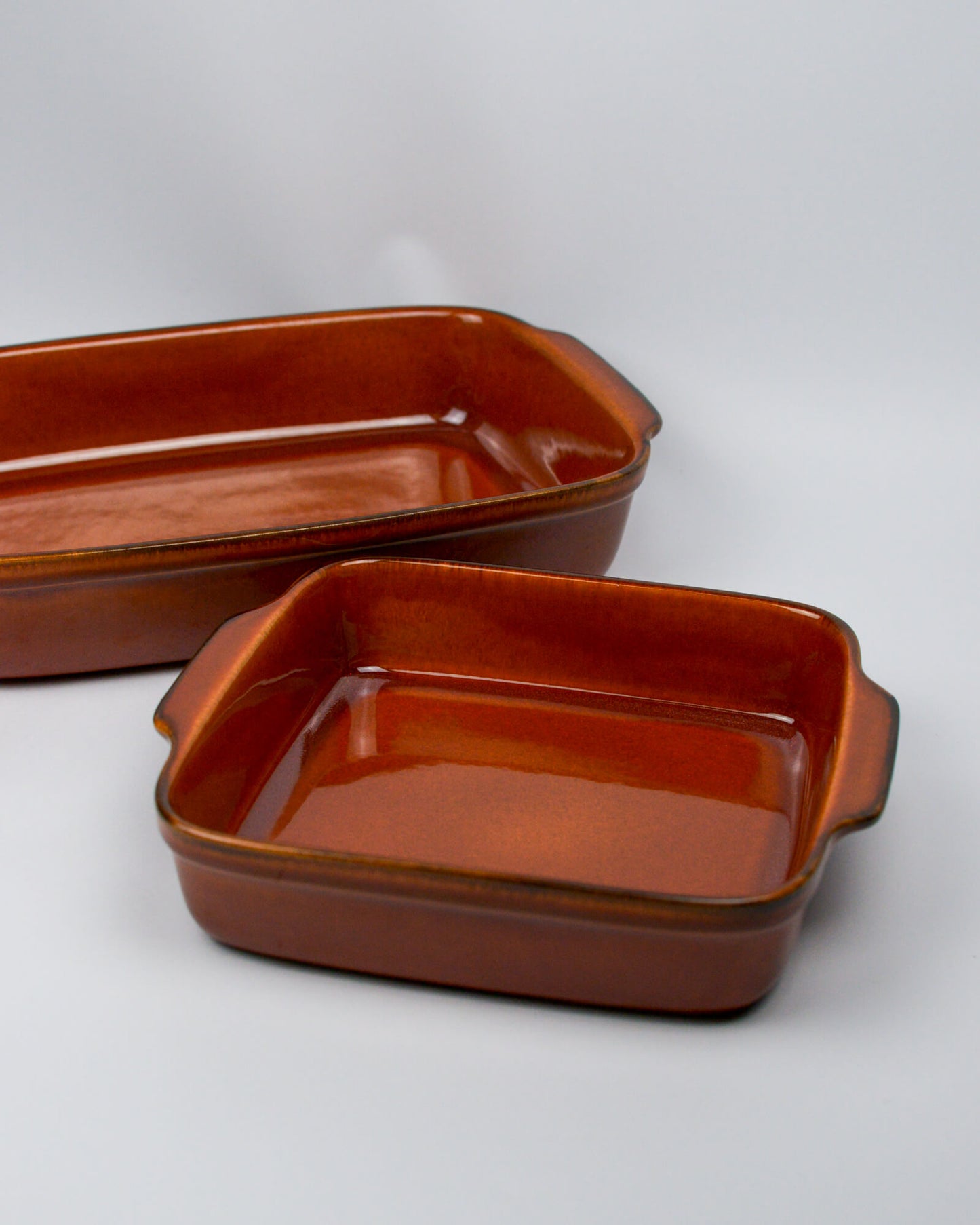 Two burnt orange ceramic baking dishes on a white background similar in style to le cruset