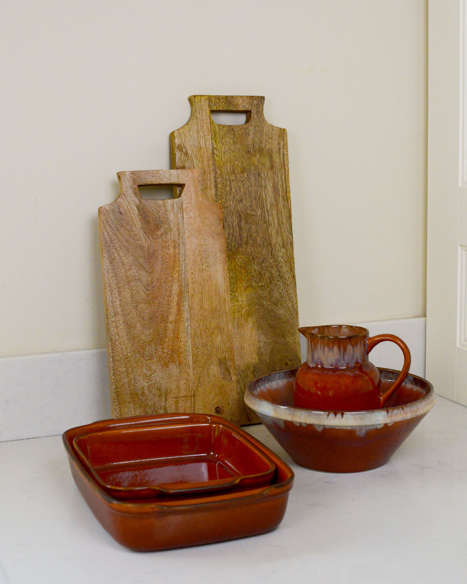 Set of caramel coloured ceramic dishes including a bowl, square dish, and pitcher on a white surface.