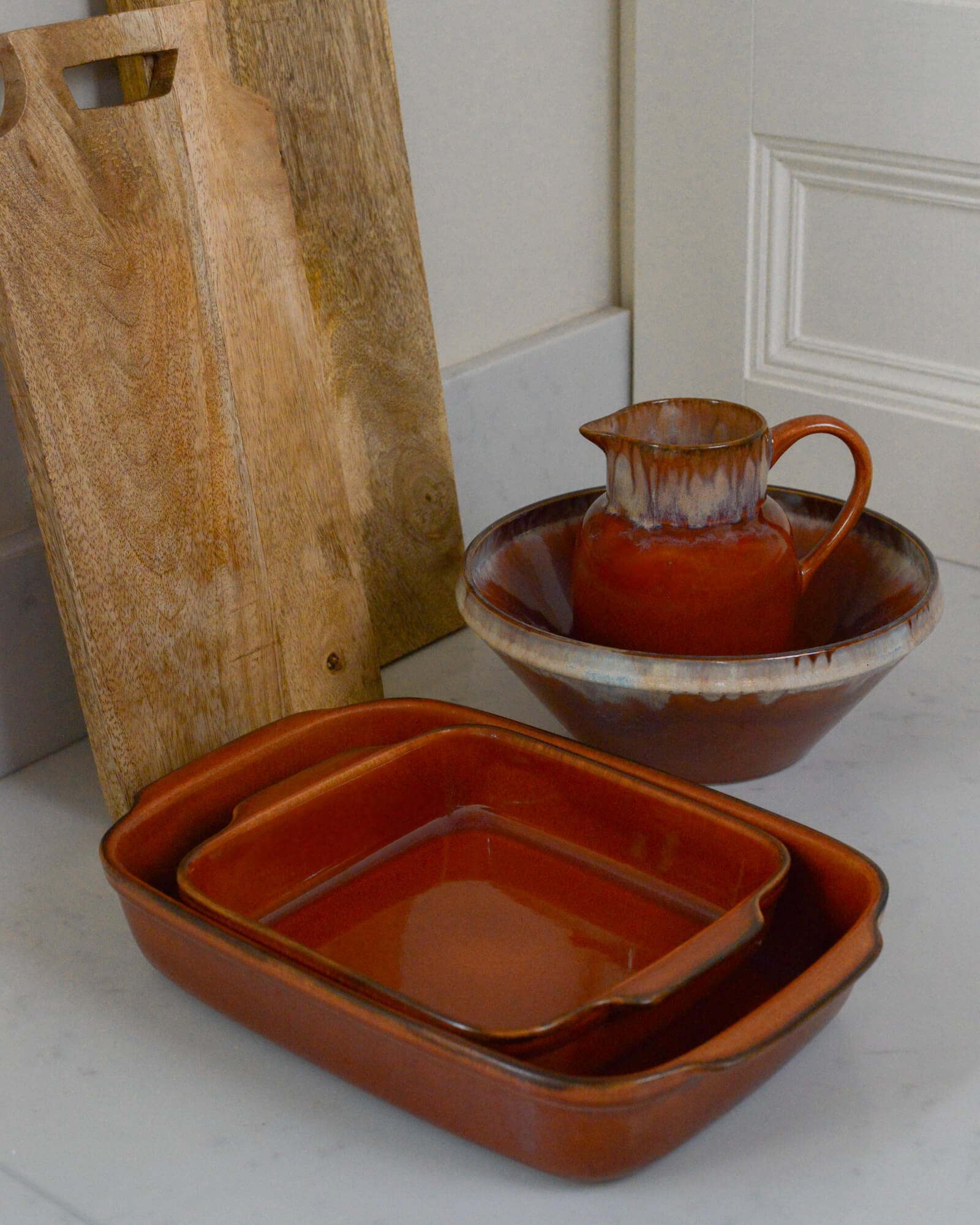 Set of caramel brown ceramic cookware including a bowl, pitcher, and rectangular dish on a white marble surface.