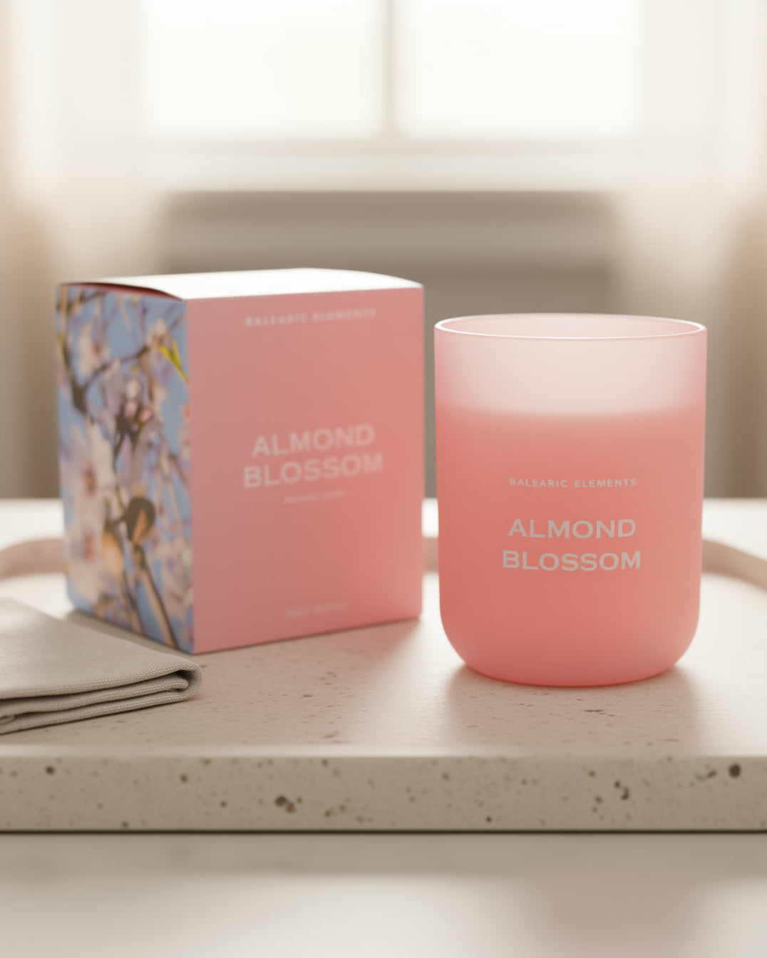 Pink 'Almond Blossom' scented candle and packaging on a light surface with a blurred background