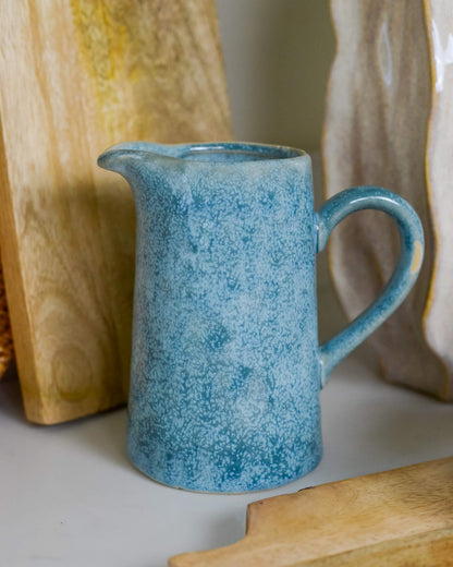 Blue ceramic pitcher on a marble surface with wooden grazing board in the background