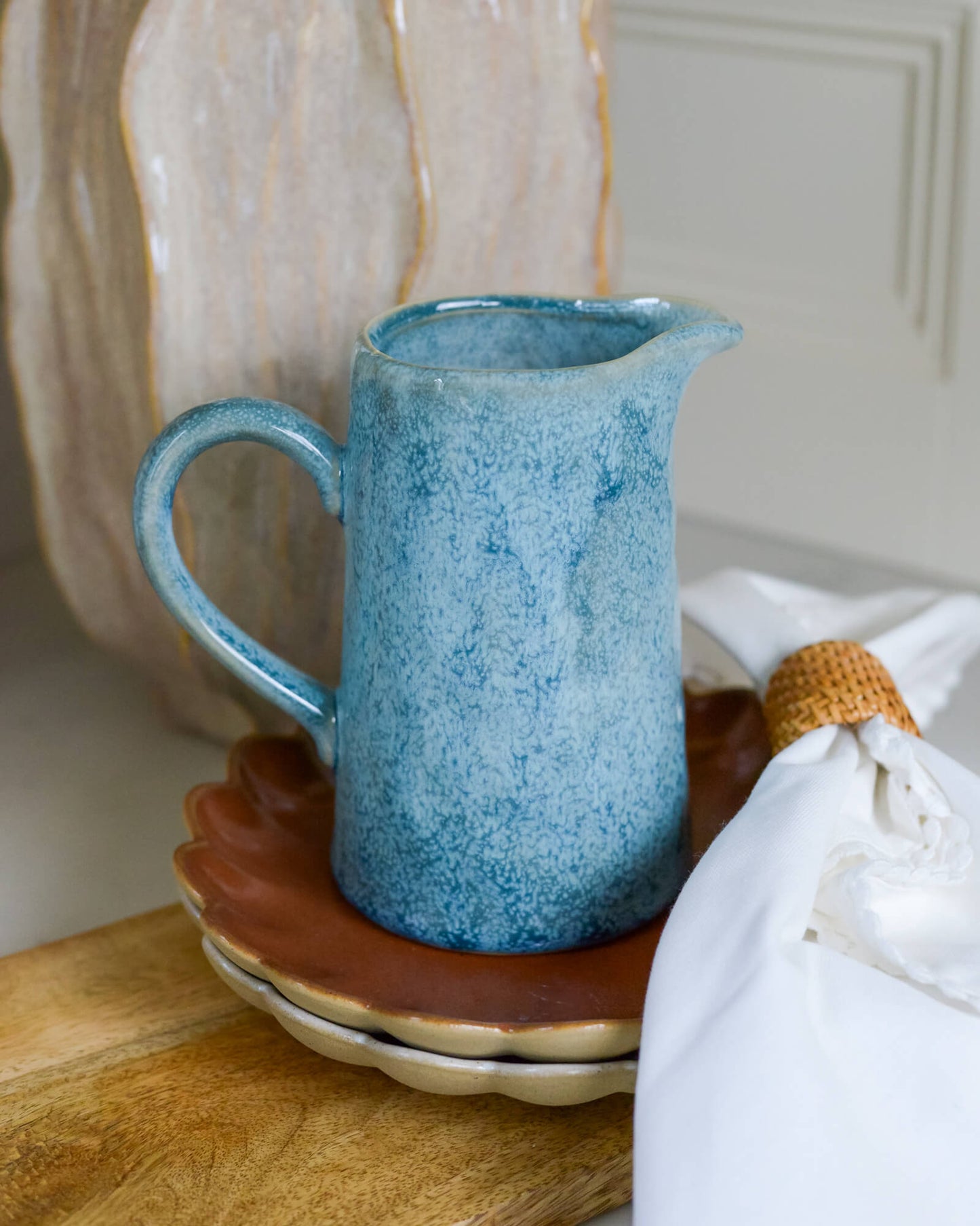 Blue ceramic pitcher on a wooden surface with a white cabinet in the background