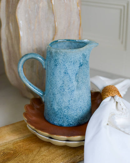 Blue ceramic pitcher on a wooden surface with a white cabinet in the background