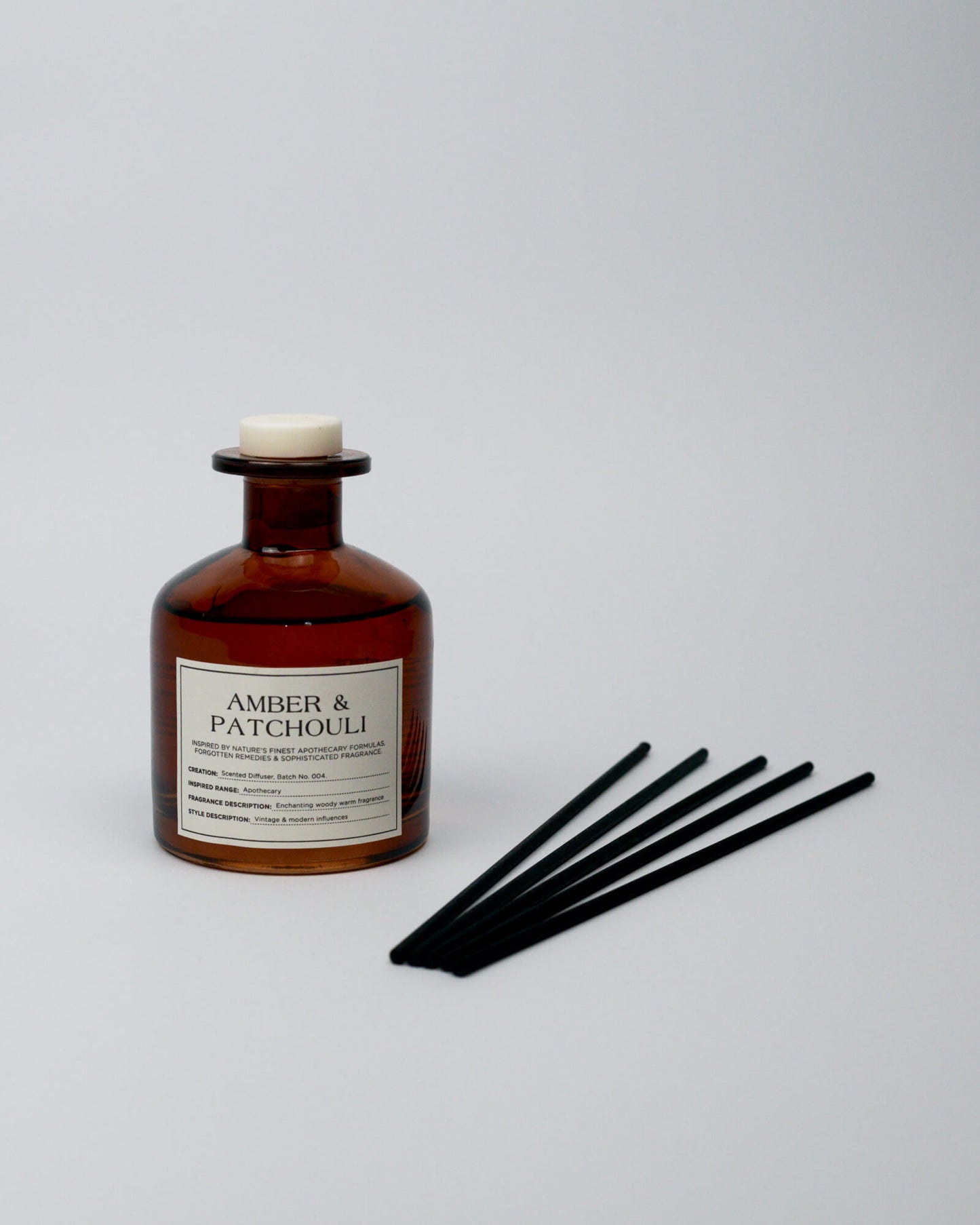 Amber and patchouli diffuser bottle with black sticks on a white background