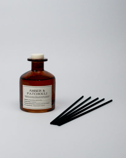 Amber and patchouli diffuser bottle with black sticks on a white background