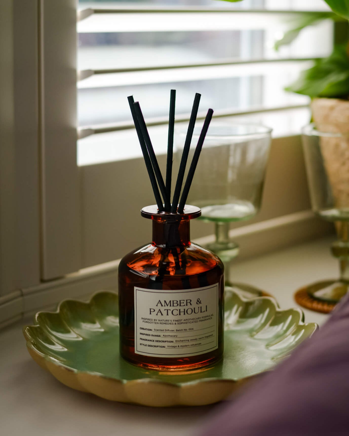 Reed diffuser labeled 'Amber & Patchouli' on a decorative tray with a blurred background