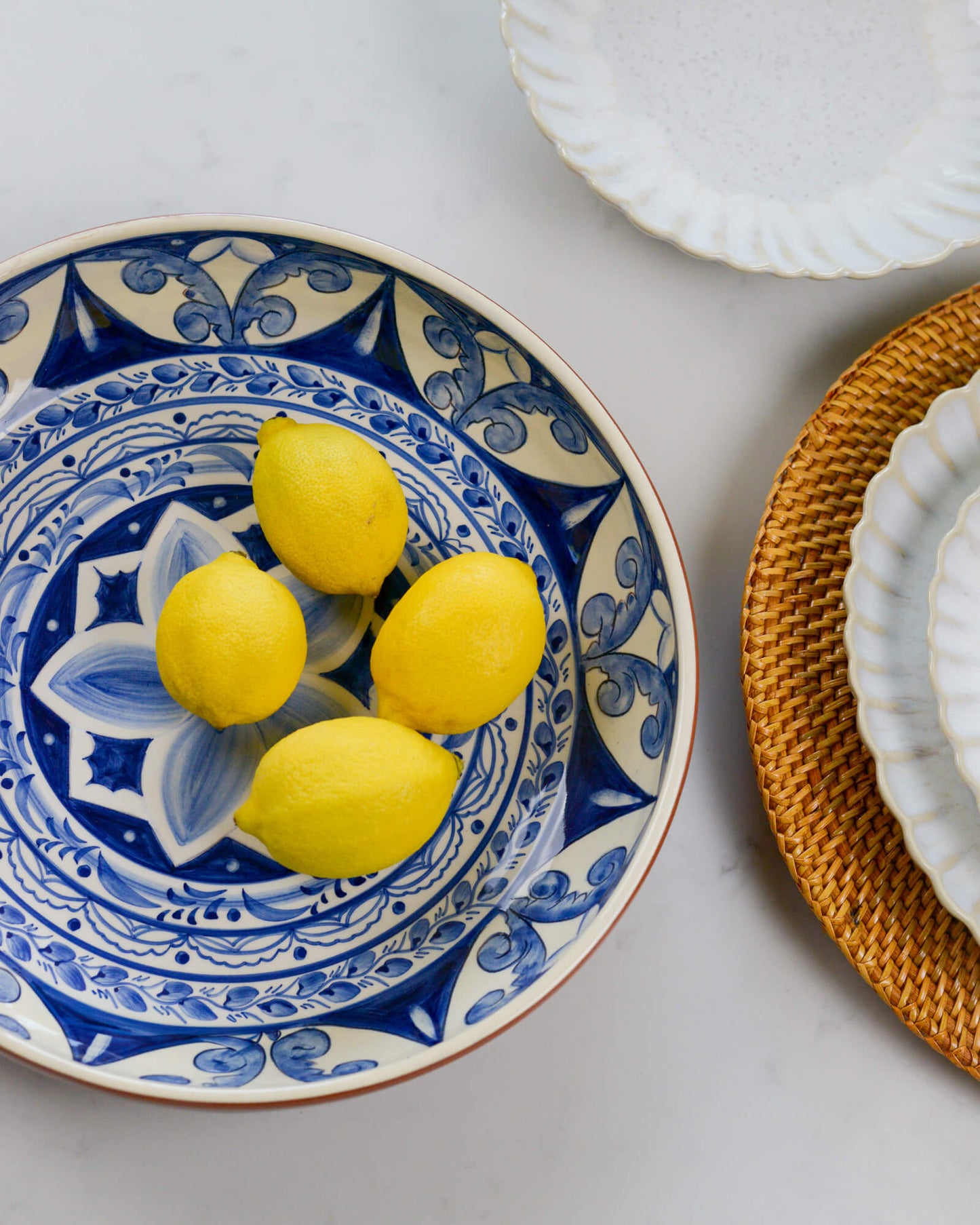 Decorative terracotta serving bowl with blue patterns holding lemons on a white surface.