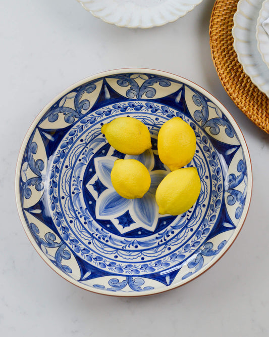 Decorative terracotta serving bowl with blue patterns holding three lemons on a light marble background