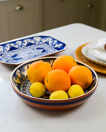 Decorative terracotta bowl of oranges and lemons on a table with decorative plates in the background