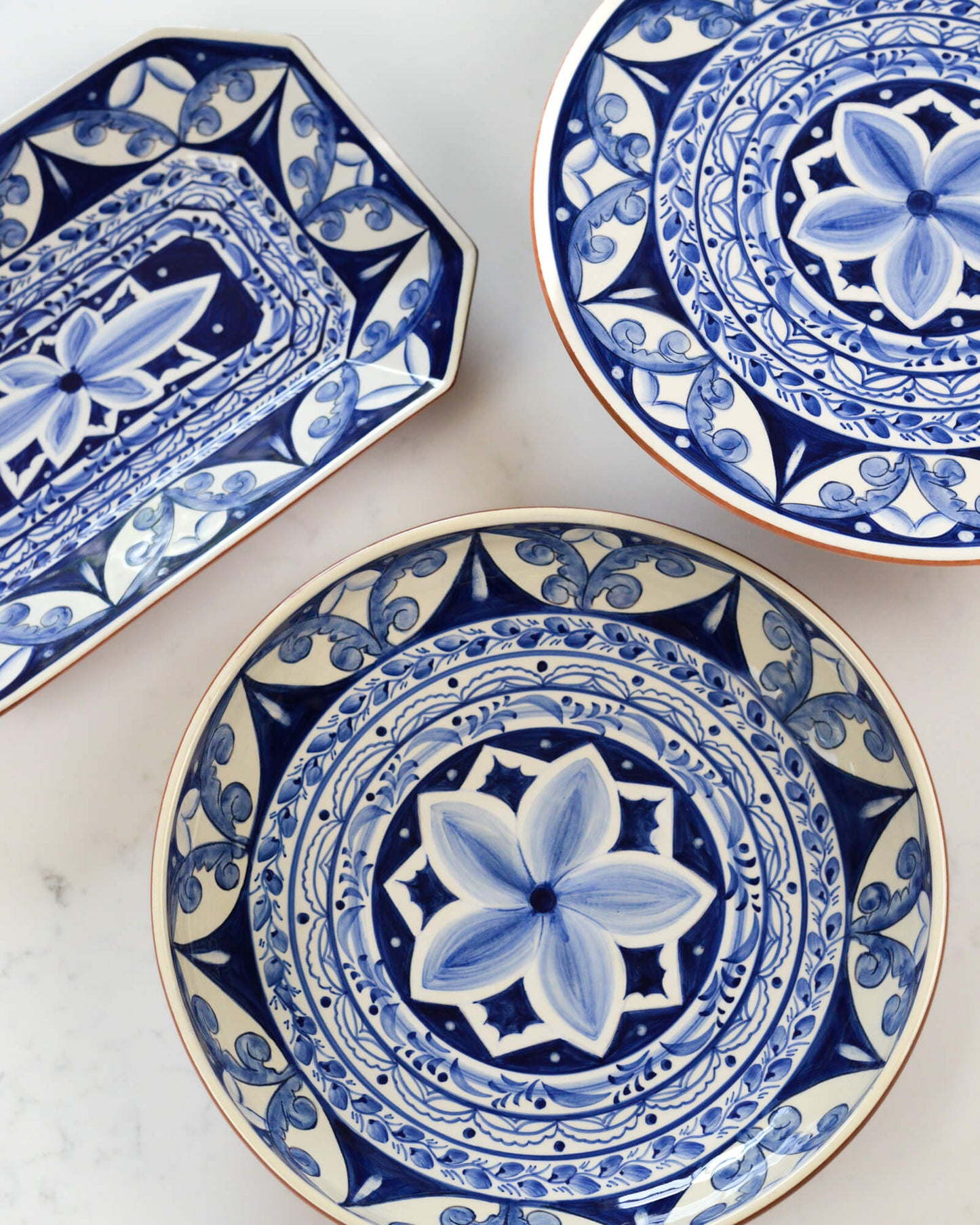 Three blue and white terracotta ceramic plates with intricate patterns on a marble surface.