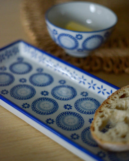 Decorative blue and white plate with a bowl and bread on a wooden surface