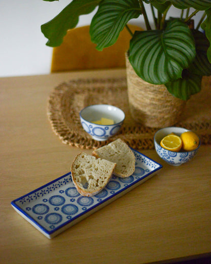 Bread on a decorative rectangular plate with a bowl of lemons and a cup on a wooden table.