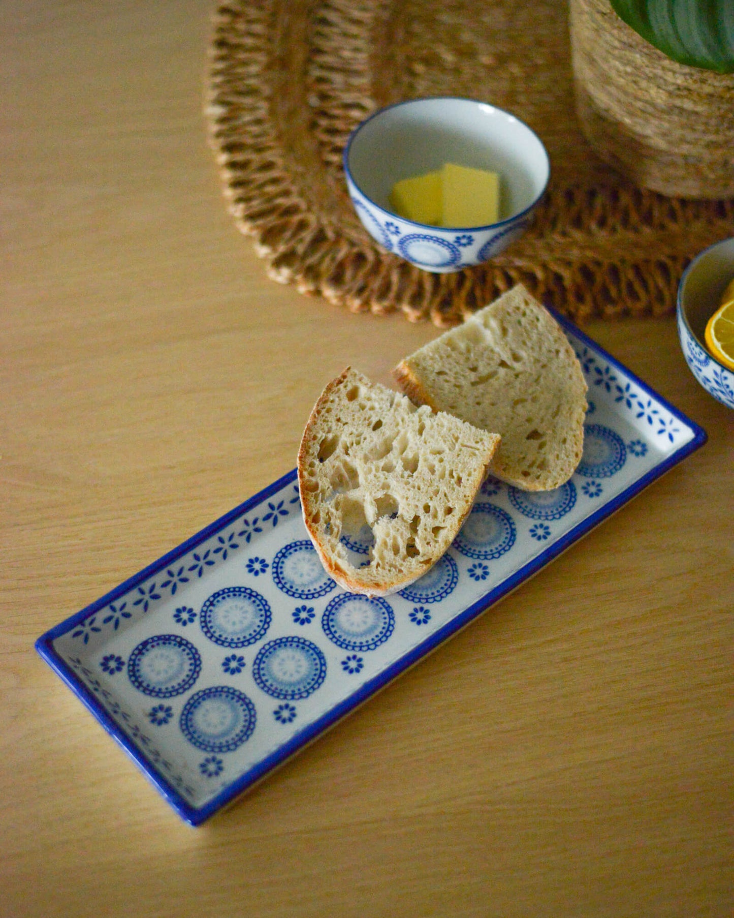 Sliced bread on a decorative rectangular serving plate with a bowl of butter in the background