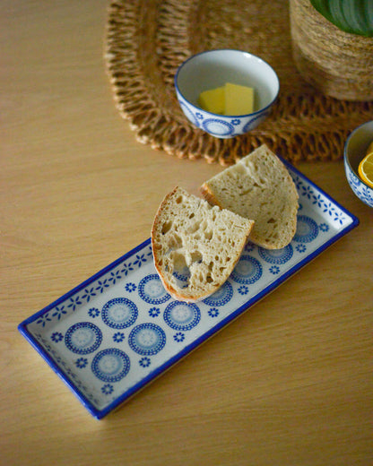 Sliced bread on a decorative rectangular serving plate with a bowl of butter in the background