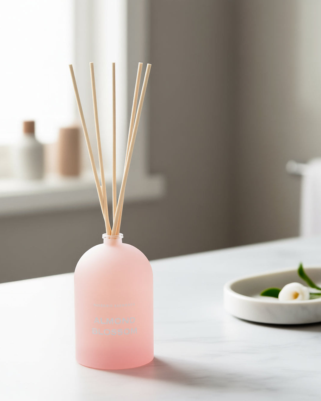 Pink diffuser bottle with wooden sticks on a white surface