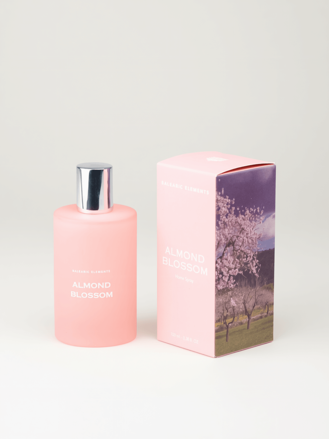A pink bottle of Almond Blossom room spray next to its matching pink packaging box featuring a cherry blossom tree illustration, set against a plain light gray background.