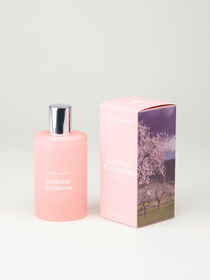 A pink bottle of Almond Blossom room spray next to its matching pink packaging box featuring a cherry blossom tree illustration, set against a plain light gray background.