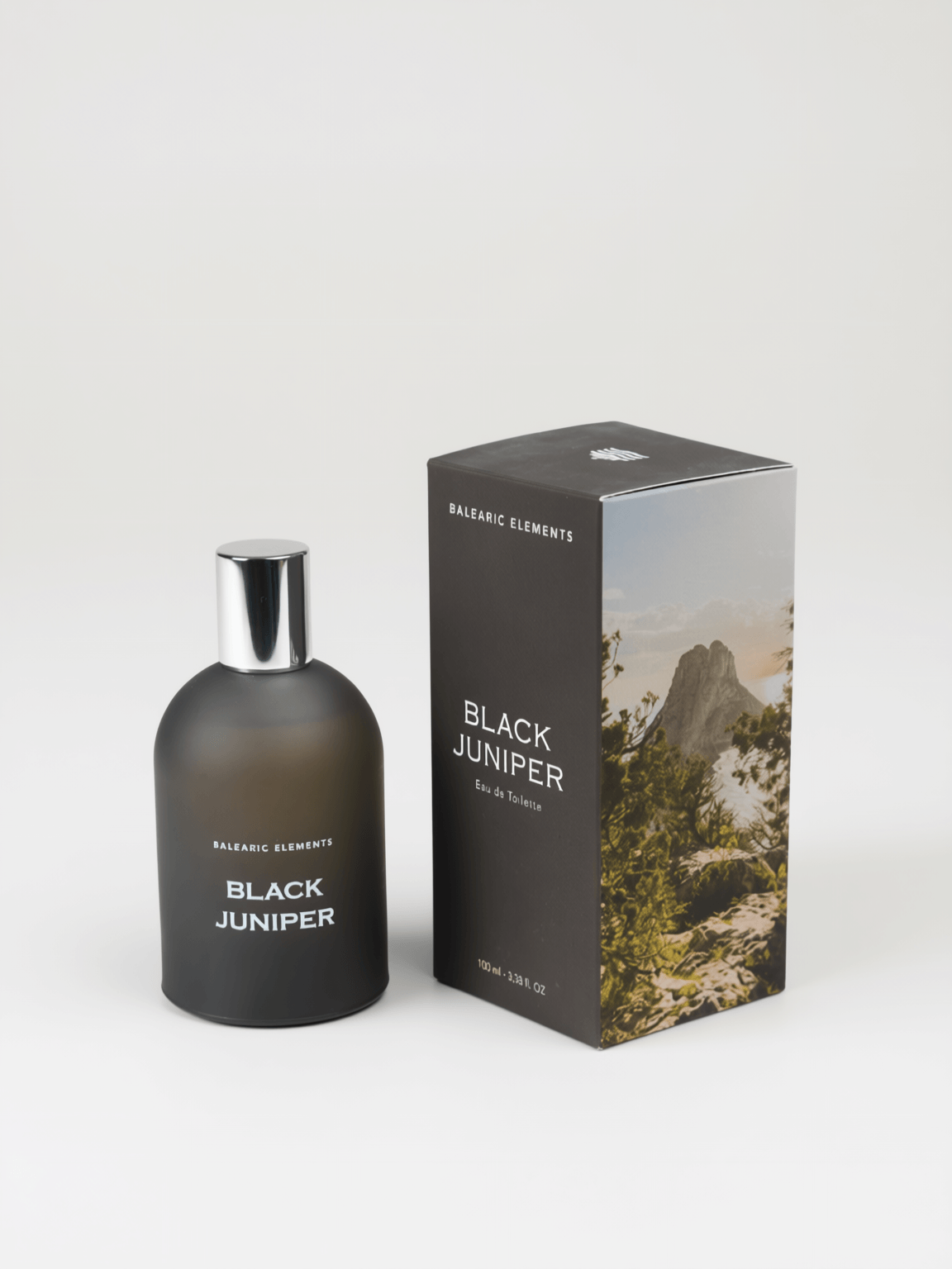 A bottle of Balearic Elements Black Juniper cologne next to its packaging box, featuring a dark smoky bottle and a box with a mountain landscape print on a light gray background.