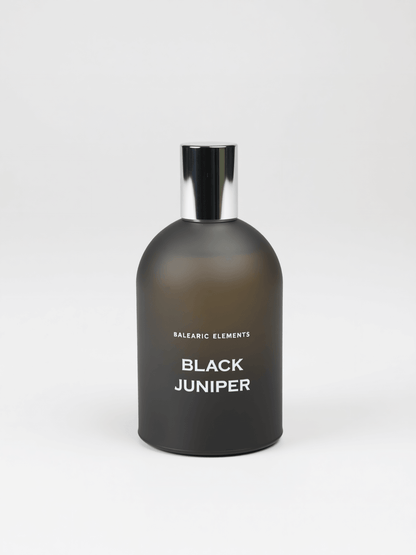 A matte black glass perfume bottle with a reflective silver cap, labeled 'BALEARIC ELEMENTS BLACK JUNIPER' in white text, set against a clean light gray background.