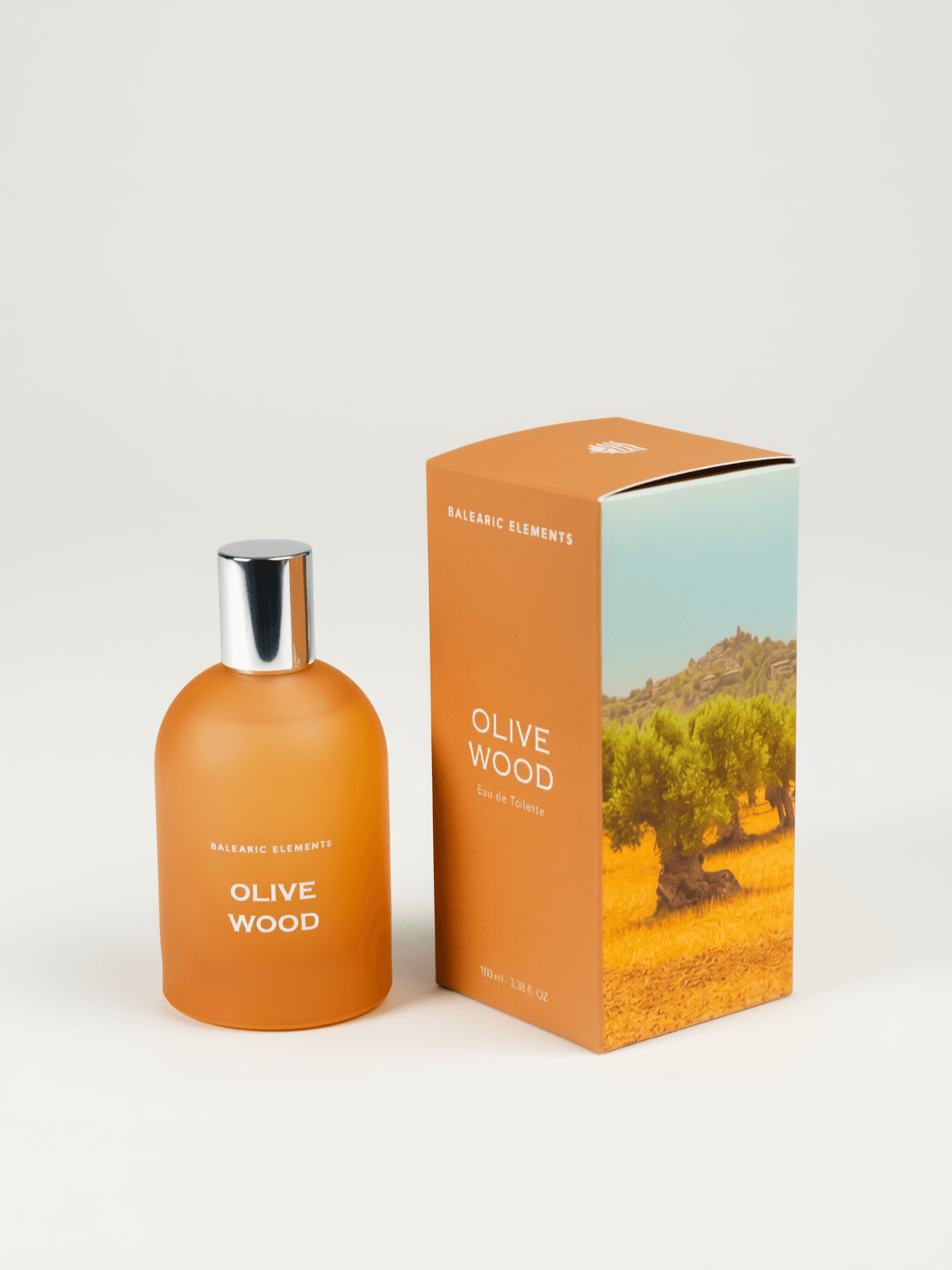 An orange frosted glass bottle with a shiny silver cap, next to it's box, labeled 'OLIVE WOOD' by Balearic Elements, set against a plain white background.