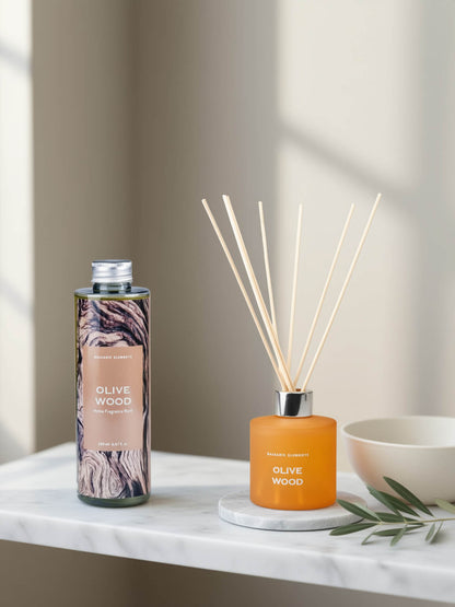 Olive Wood reed diffuser set by Beautifully Scented, featuring a patterned glass bottle and an amber glass reed diffuser bottle with wooden reeds, styled on a white marble surface next to a ceramic bowl.
