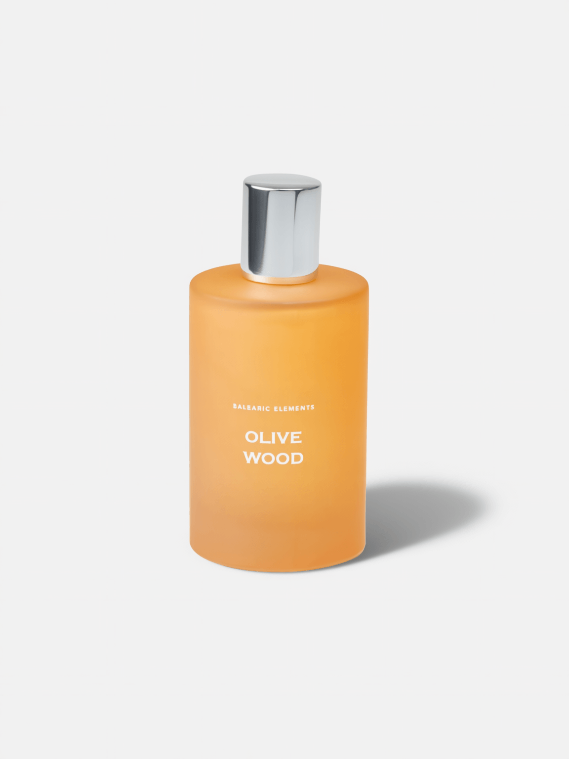 An orange frosted glass bottle with a silver metallic cap, labeled 'OLIVE WOOD' and 'BALEARIC ELEMENTS', on a light grey background.