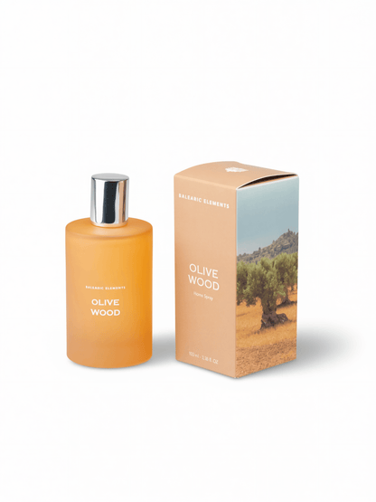 A bottle of olive wood fragrance with a silver cap next to its peach-colored packaging box featuring an olive tree landscape print, on a white background.