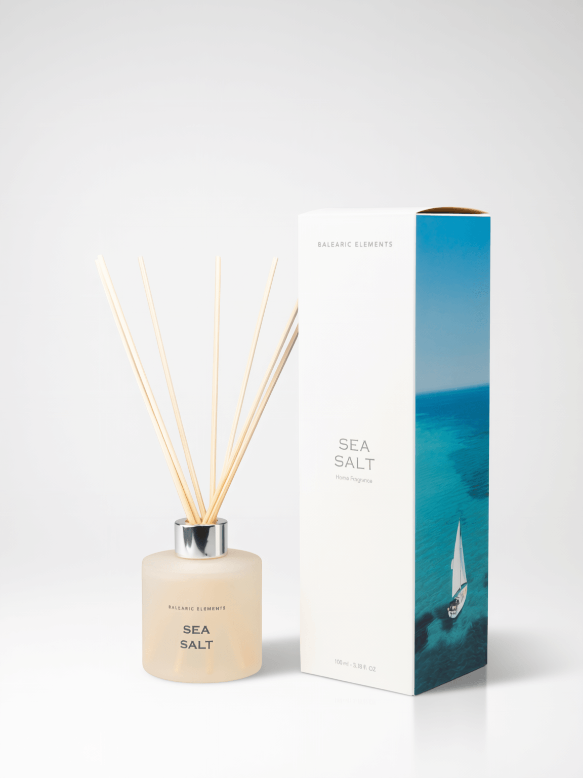 A reed diffuser bottle with natural reeds next to its white and blue packaging box, labeled 'SEA SALT' by Balearic Elements, on a white background.