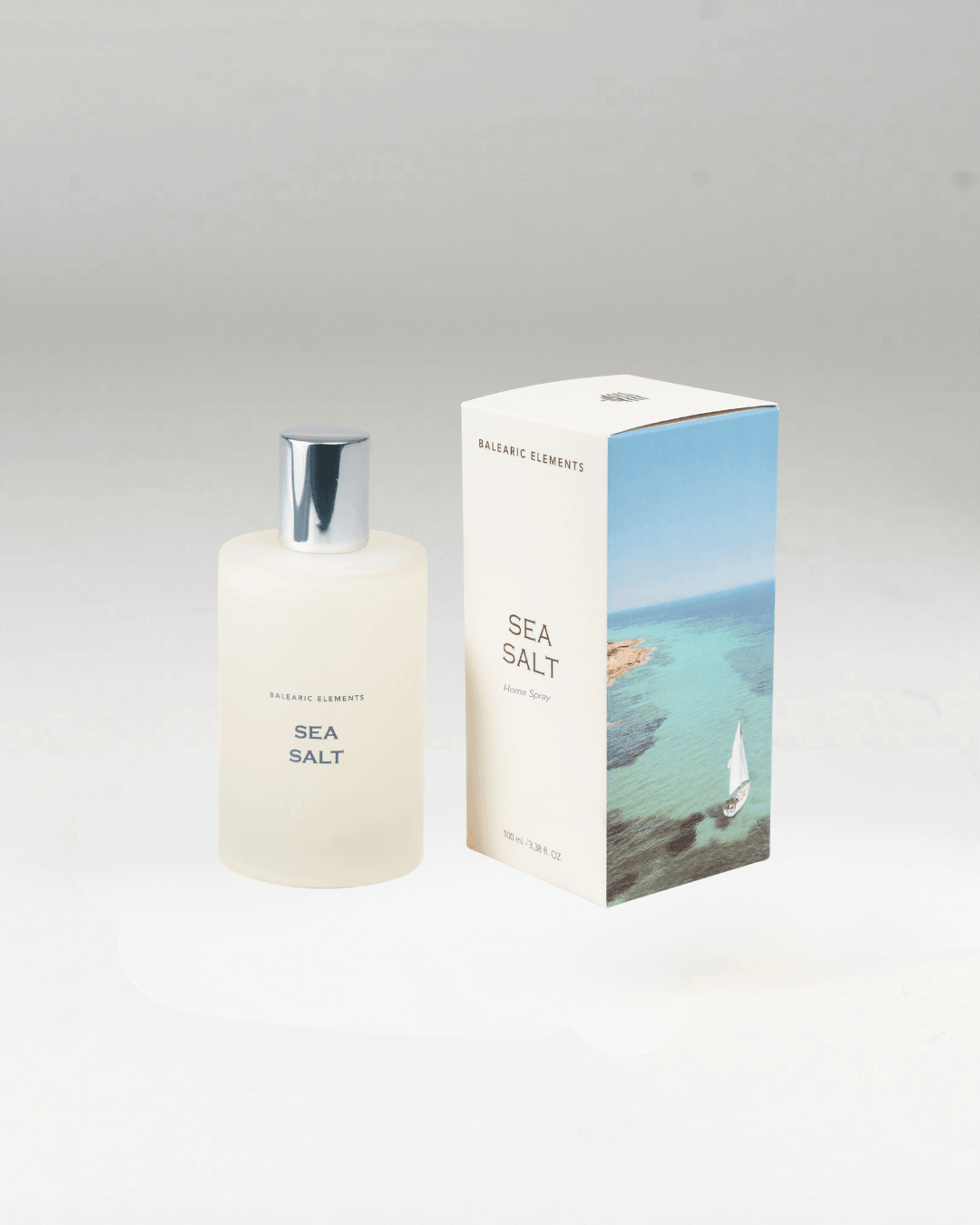 A frosted glass bottle of Balearic Elements Sea Salt perfume with a silver cap, standing next to its white packaging box featuring a blue sea and sailboat illustration.
