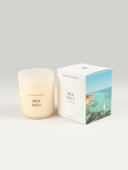 A sea salt scented candle by Balearic Elements in a frosted glass jar, shown next to its white packaging box featuring a coastal illustration.